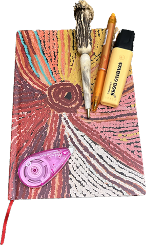 A patterned notebook with an antler pen, an orange pen, a highlighter and correction tape
